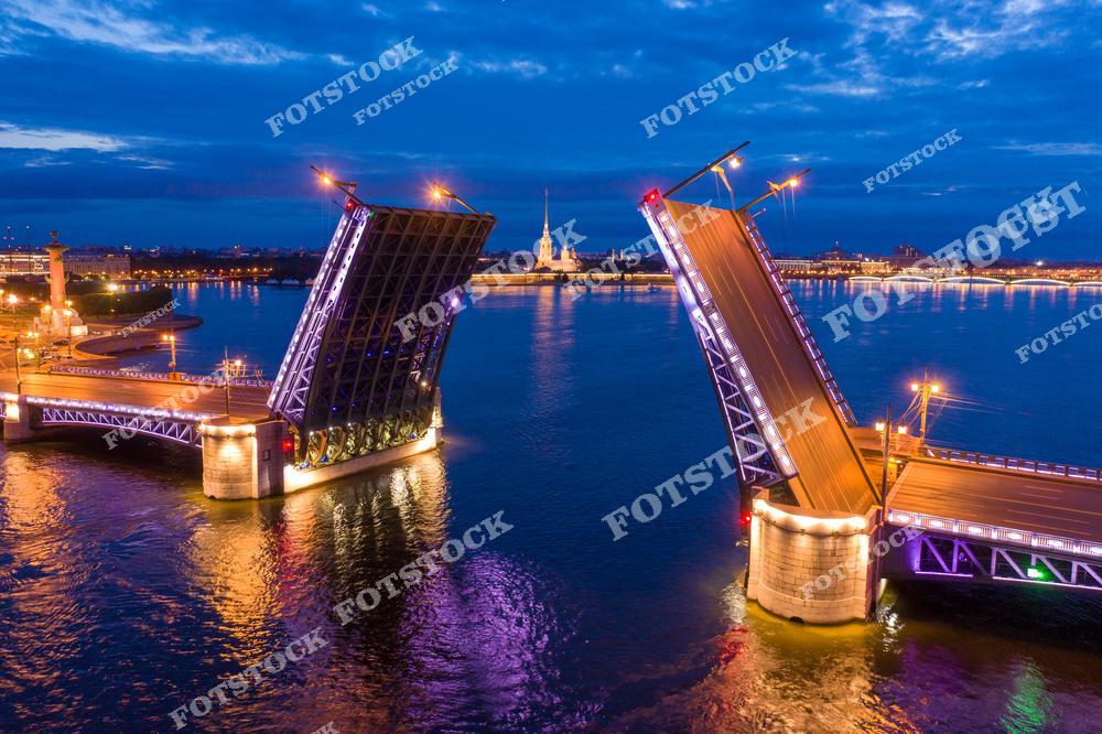 Фотография вечернего Санкт-Петербург, Россия, снятая с высоты. На изображении запечатлена река Нева и разведённый Дворцовый мост, являющийся одним из главных символов города. Фотоснимок передаёт панораму вечернего Петербурга: огни набережных, отражения в воде и величественную атмосферу города рек и мостов. Фото подчёркивает уникальный облик Санкт-Петербурга и красоту вечерних городских пейзажей. Иллюстрация может использоваться как изображение, картинка или слайд, посвящённые рекам, мостам и панорамам российских городов.